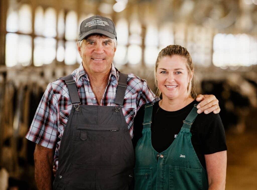 Father and daughter standing together in a dairy cow barn